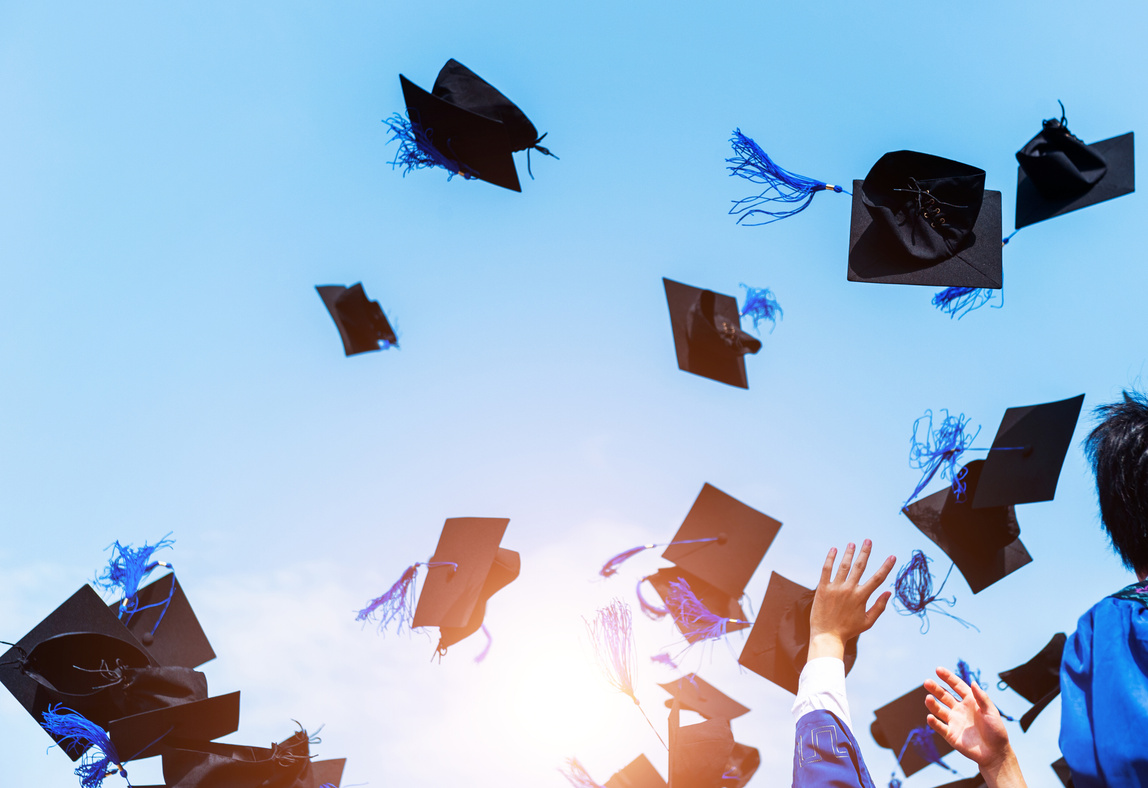 Graduating students hands throwing graduation caps in the air